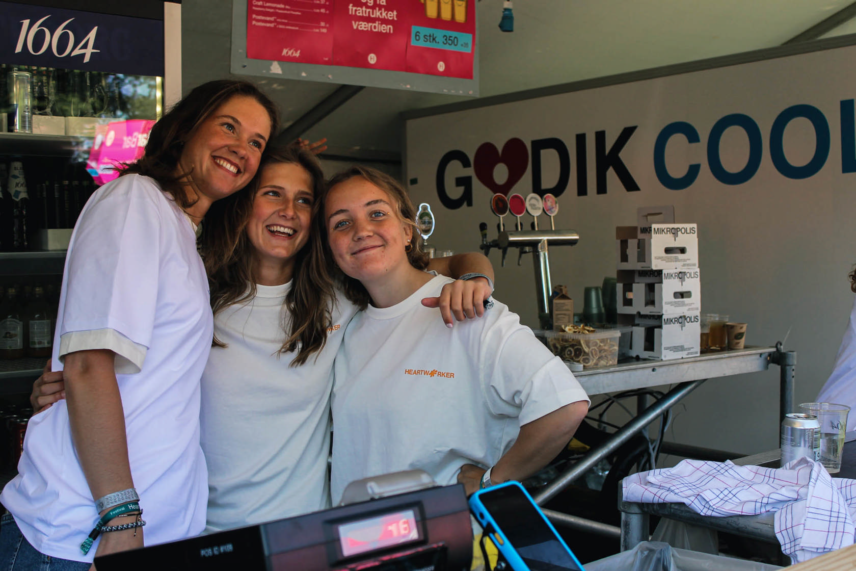 Tre frivillige bartendere på en festival står foran en Godik kølevogn 