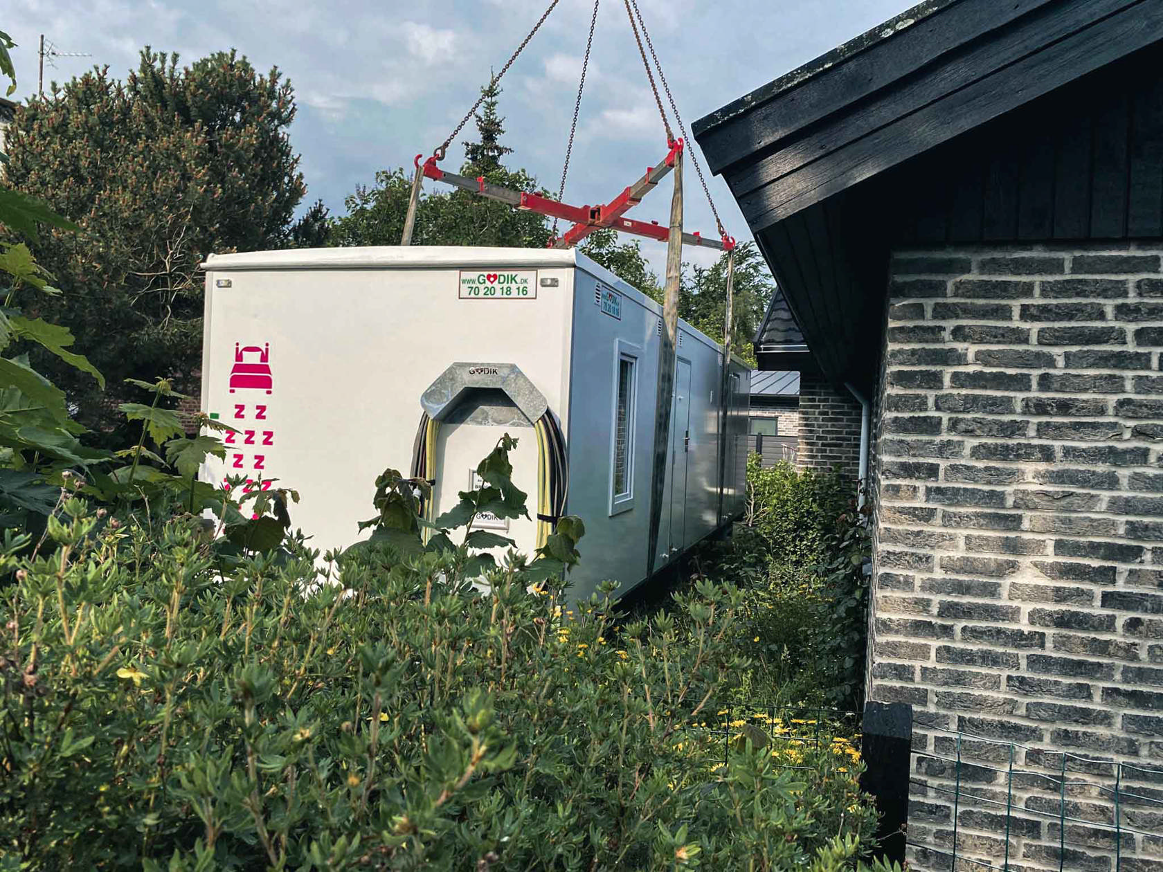 En beboelsesvogn bliver flyttet over hækken og placeret i haven til et parcelhus