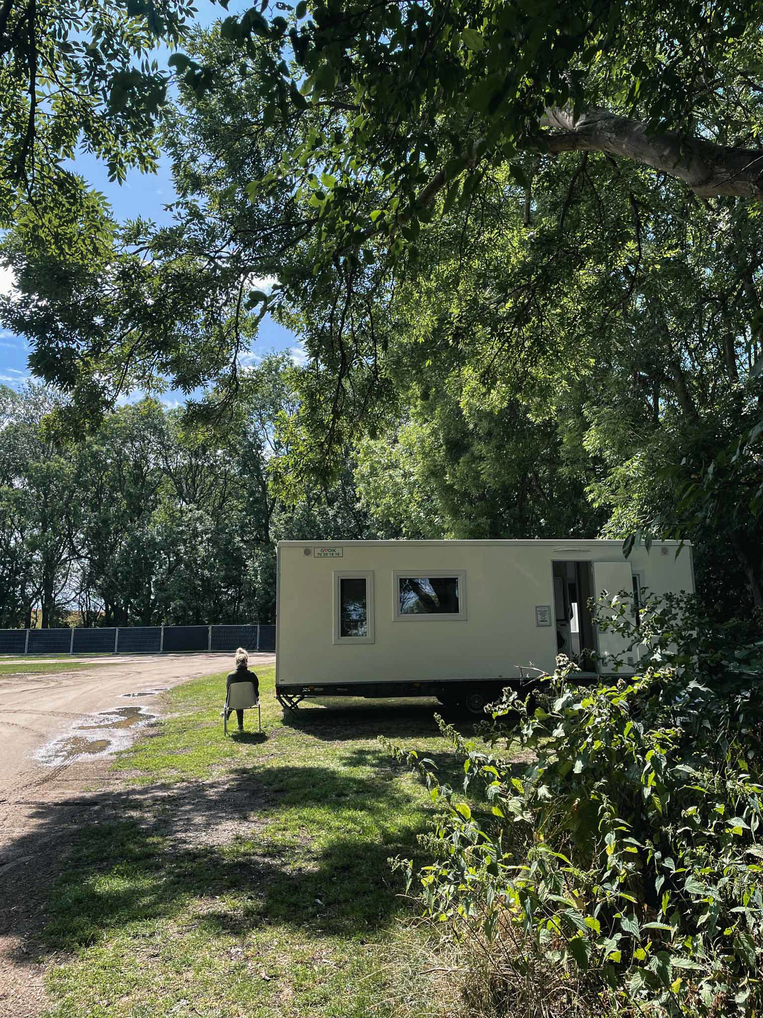 En kvinde sidder på en stol i skovbrynet ved siden af en Godik beboelsesvogn
